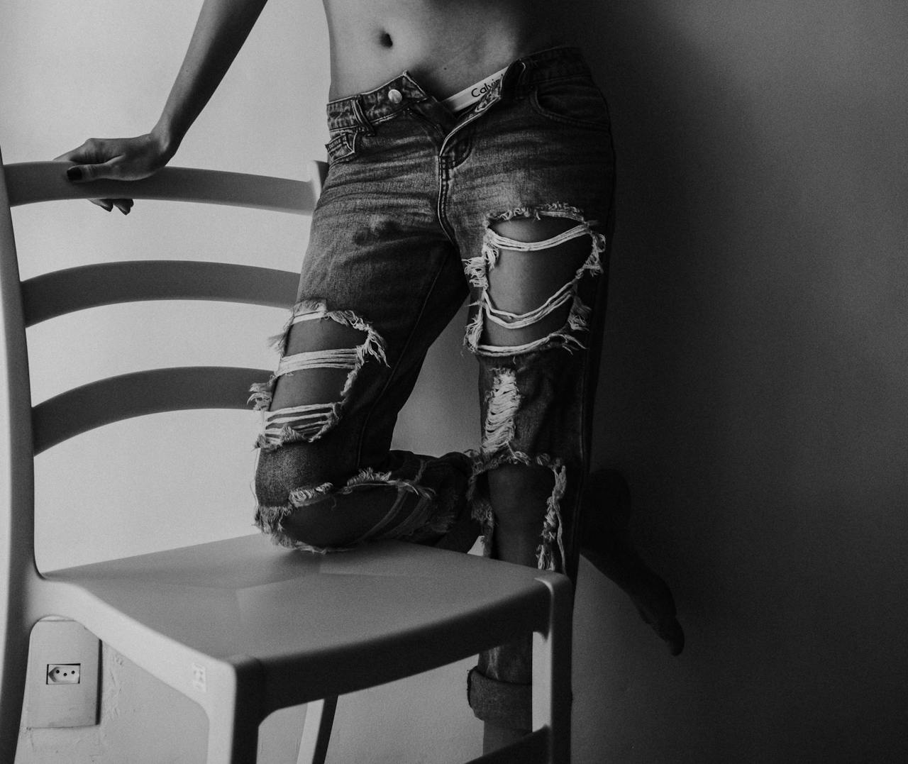 Stylish black and white photo of ripped jeans with a modern chair, showcasing trend and style.
