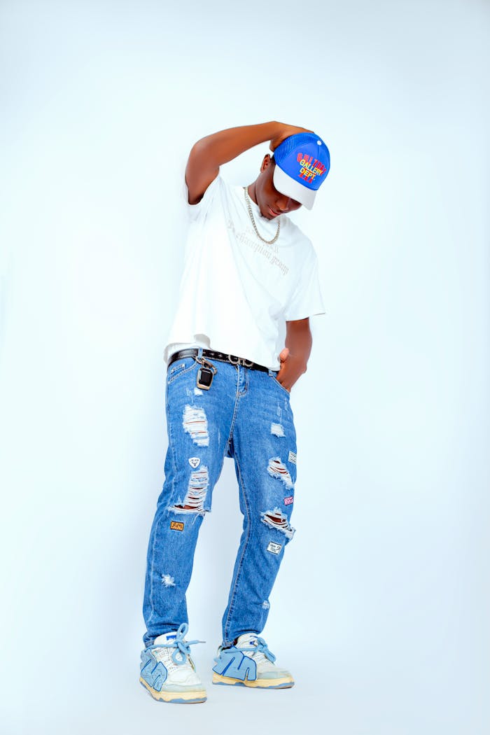 Teenager in trendy jeans and cap posing against white background.